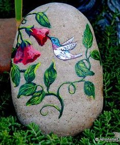 a painted rock sitting in the grass with flowers on it and a bird flying over it