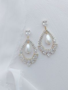 a pair of earrings with white pearls and crystal stones on the bottom, sitting on a white cloth