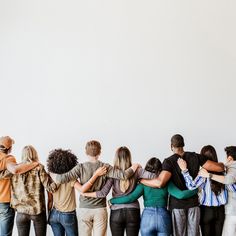 a group of people standing next to each other in front of a white wall with their arms around each other