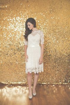 a woman standing in front of a gold sequin wall with her hands on her hips