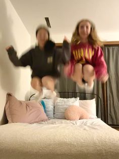 two girls jumping on a bed with pillows