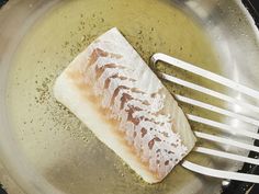 a piece of fish sitting on top of a frying pan next to a fork