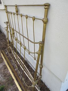 a gold metal bed frame sitting in front of a white building with grass and dirt on the ground