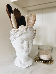 a white statue head sitting on top of a counter next to a jar filled with wooden spoons