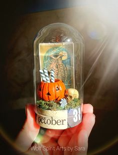 a person holding up a glass jar filled with fake pumpkins and other things in it