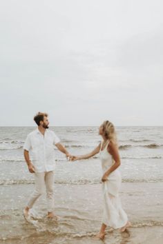 a man and woman holding hands while walking on the beach