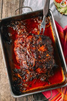 a meat dish in a pan with a fork on the side and some vegetables next to it