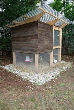 a chicken coop in the middle of some grass and gravel with two chickens inside it