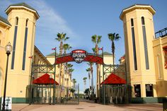 an entrance to a sports complex with palm trees in the background and a red gate