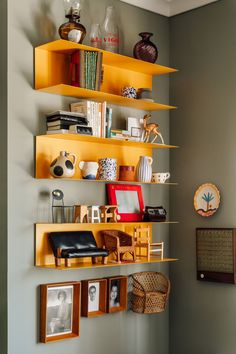 a yellow shelf in the corner of a room with pictures and other items on it