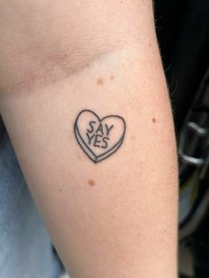 a small heart tattoo on the arm saying say yes