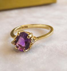 a gold ring with an amethorate and two diamonds on the side, sitting on a white surface