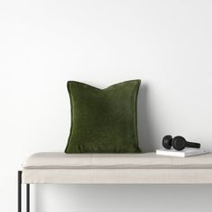 a green pillow sitting on top of a white bench next to a book and headphones