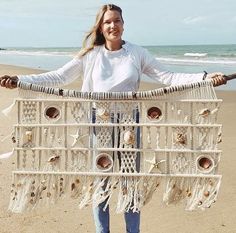 a woman standing on the beach holding up a large piece of art made out of shells