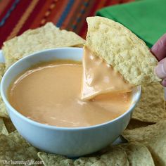 a person dipping tortilla chips into a white bowl filled with melted caramel sauce