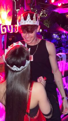 a man in a crown is hugging a woman's head at a party with neon lights behind him