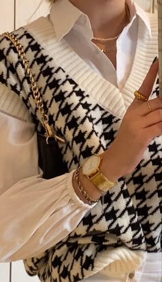 a woman in white shirt and black and white sweater with gold bracelets holding up her hand