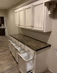 an empty laundry room with white cabinets and baskets on the bottom shelf in front of it