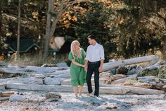 a man and woman walking on the beach holding hands with trees in the back ground