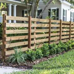 a wooden fence in front of a house with grass and bushes growing on the side