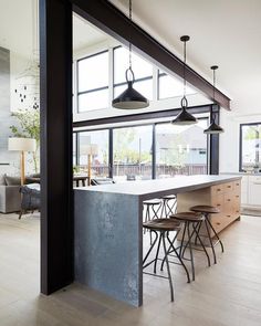 an open kitchen and living room with large windows in the center, along with bar stools that sit on hard wood flooring