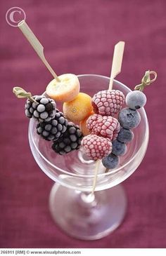 a glass filled with fruit on top of a purple table next to a pink wall