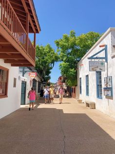 people are walking down the street in front of some buildings and trees on a sunny day