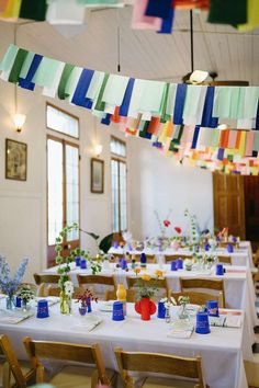 a room filled with tables covered in white tablecloths and colorful streamers hanging from the ceiling