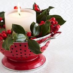 a candle in a red colander with holly and berries