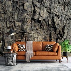 a brown couch sitting in front of a wall covered in rocks and other furniture next to a lamp