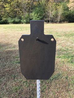 a black sign sitting on top of a metal pole in the middle of a field