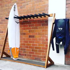 a surfboard is propped up against a brick wall next to a coat rack and jacket hanger