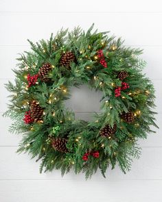 a wreath with pine cones and red berries hanging on a white wall next to a brick wall