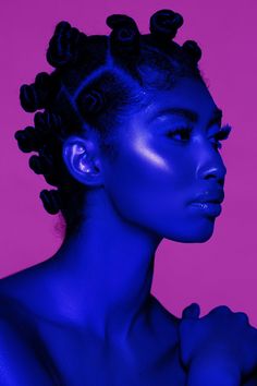 a woman with blue powder on her face and hair in buns, against a pink background