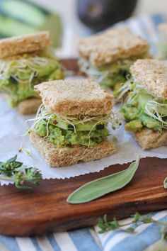 several sandwiches on a wooden cutting board with sprouts and leaves next to them