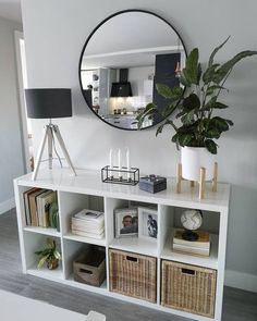 a white bookcase with baskets and plants on it in front of a round mirror