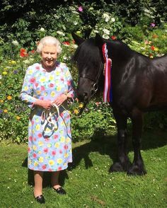 an older woman standing next to a black horse in a flowery garden with flowers