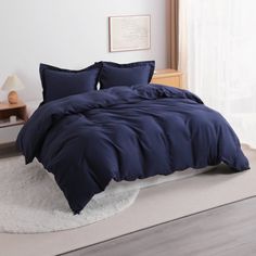 a bed with blue comforter and pillows in a room next to a white rug