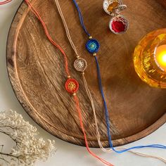 a wooden tray with three different colored beads and a candle on it next to some flowers