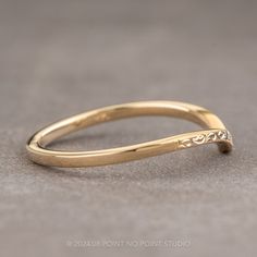 a yellow gold wedding band with an engraved design on the side, sitting on a gray surface