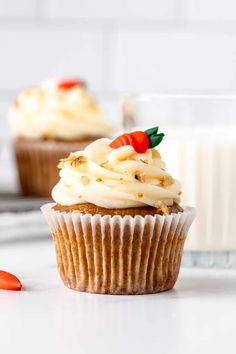 two cupcakes sitting on top of a table next to a glass of milk