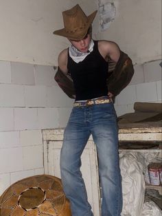 a man in jeans and a cowboy hat leaning against a wall with his hands on his hips