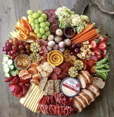 a platter filled with meats, cheeses and vegetables on top of a wooden table