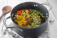 a pot filled with pasta and vegetables on top of a towel next to a wooden spoon