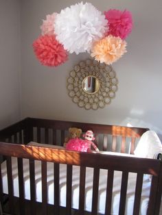 a baby crib with pink, orange and white tissue pom poms hanging from the ceiling