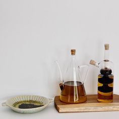 two glass jugs filled with liquid sitting on top of a wooden tray next to a bowl