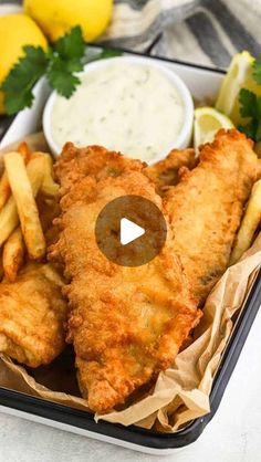 fish and chips in a tray with lemon wedges, parmesan sauce and garnishes