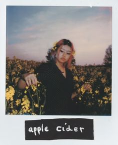 a woman with pink hair standing in a field of yellow flowers and looking at the camera