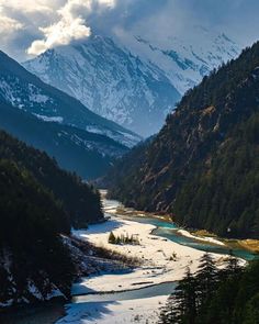 the mountains are covered in snow and green pine trees, with a river running between them