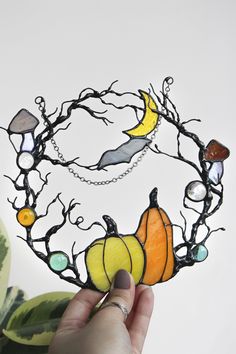 a hand holding a piece of art made out of stained glass and metal branches with pumpkins on it